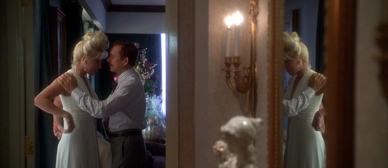 Casino (1995) movie still: medium — A hotel room features a large mirror reflecting a man and a woman. The couple faces each other while standing in…