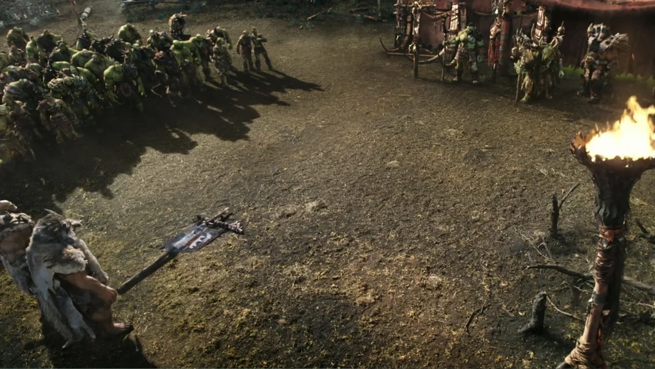 Warcraft (2016) movie still: wide — A dirt clearing serves as a gathering space for a large group of orcs. The encampment features rough tents and a…