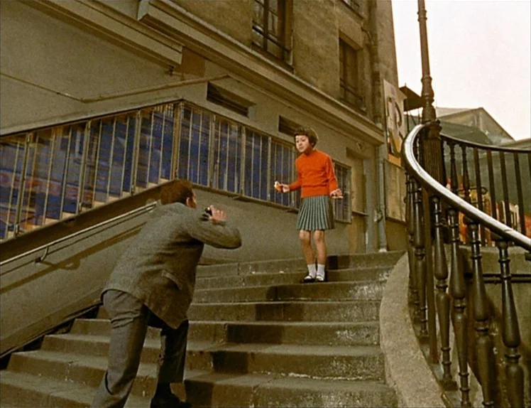 Zazie Dans Le Métro (1960) movie still: fullbody — An outdoor stone staircase sits against a Parisian-style building with iron railings. A man in a…