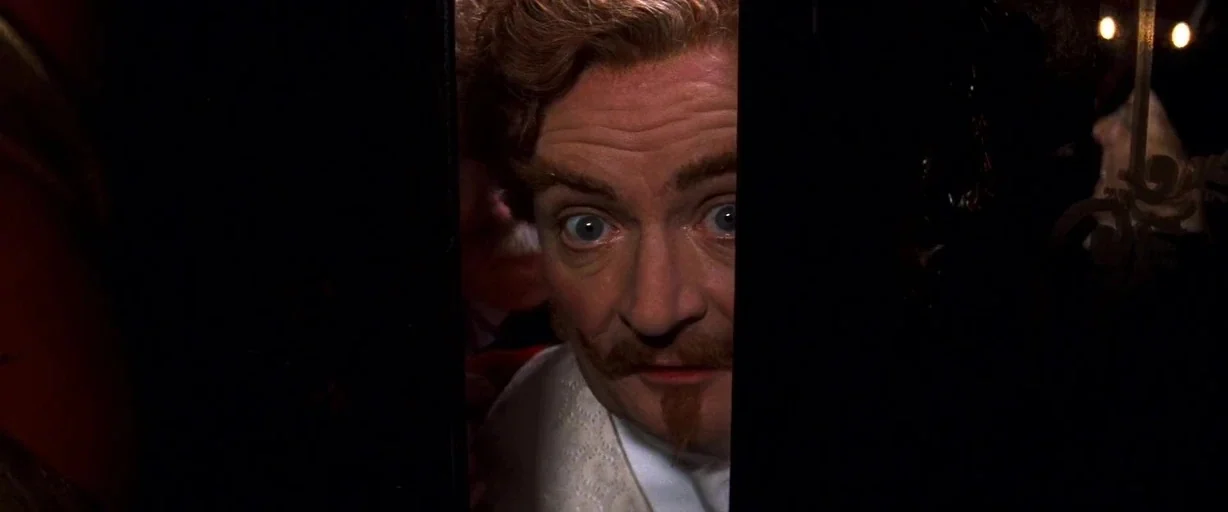Moulin Rouge! (2001) movie still: closeup — A man peers through a narrow vertical gap between two dark doors. The dark environment obscures the…