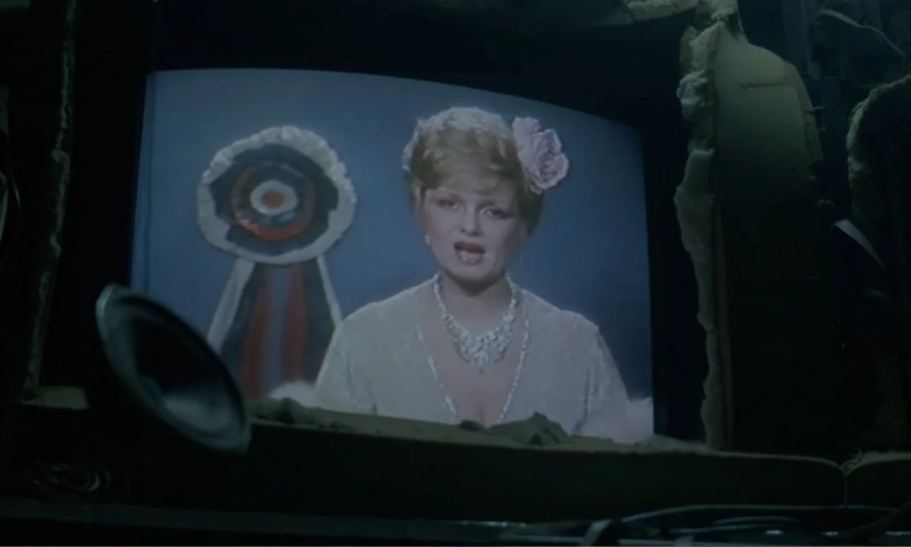 Ga-ga: Glory to the Heroes (1986) movie still: medium — A television screen displays a woman in an evening gown against a blue background. A…