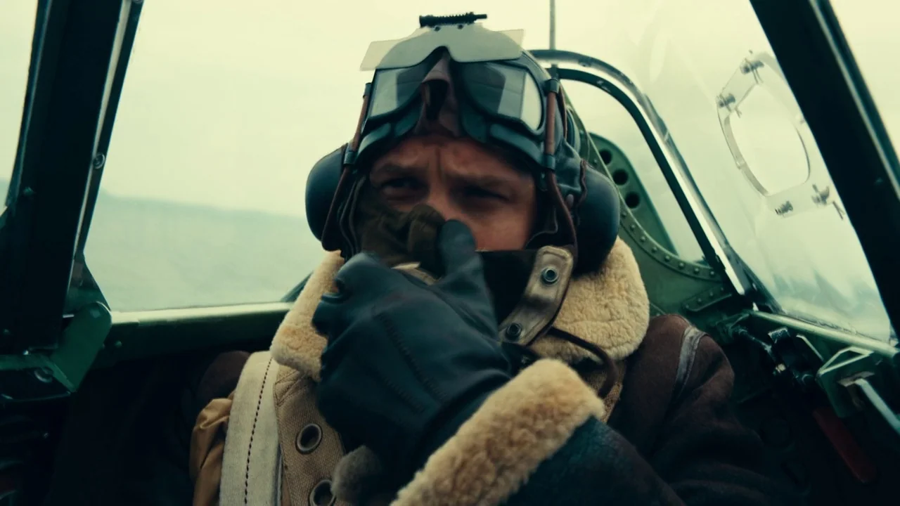 Dunkirk (2017) movie still: closeup — Inside a small World War II fighter aircraft cockpit with visible mechanical framing. A pilot in flight gear…