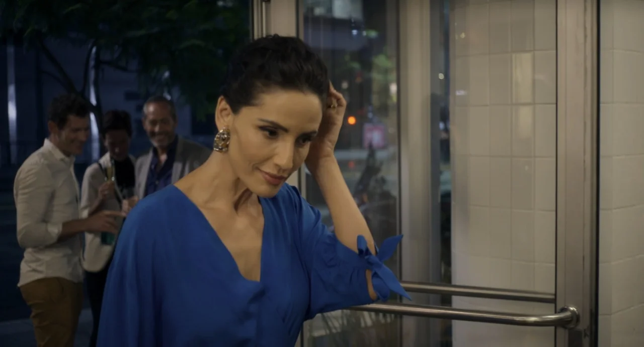 Little White Lies (2010) movie still: medium — A woman stands before a white-tiled building entrance with a glass door. Behind her, three people…