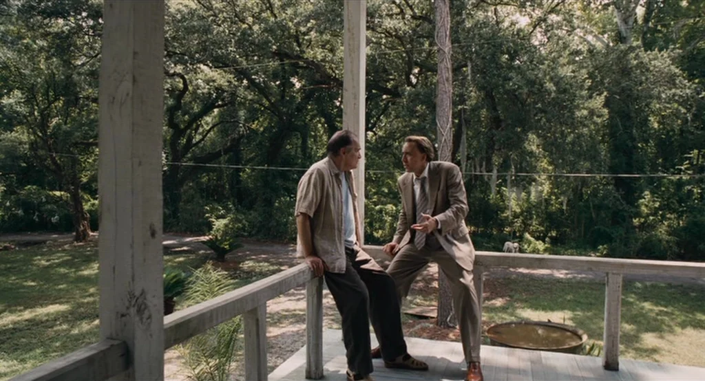 Bad Lieutenant: Port Of Call New Orleans (2009) movie still: fullbody — A wooden porch overlooks a dense, tree-covered yard under a clear sky. Two…