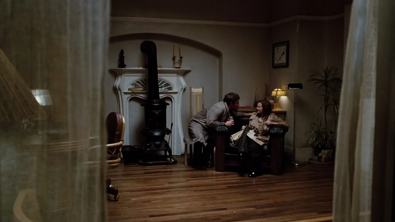 Altered States (1980) movie still: wide — A dimly lit room features a decorative fireplace with a black wood-burning stove insert. A man stands…