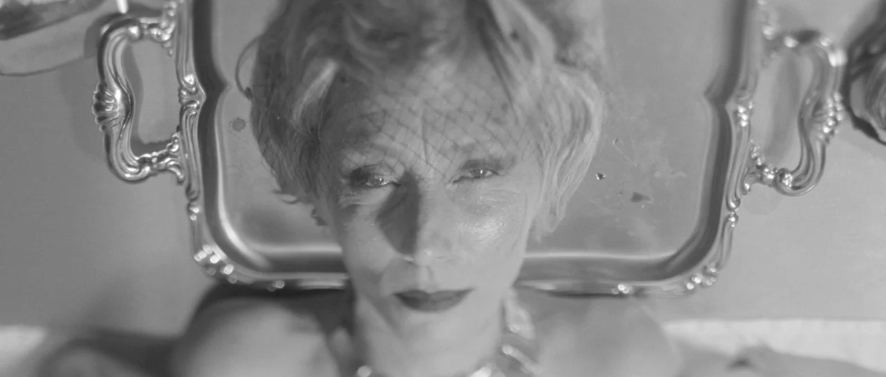 She Is Conann (2023) movie still: closeup — A close-up view shows a woman's face resting on a reflective silver tray surface. She is framed directly…