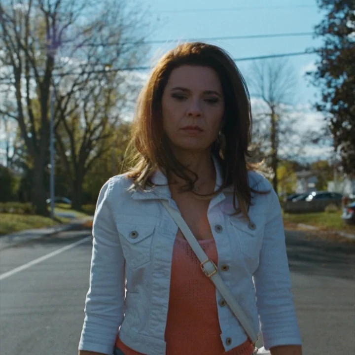 Mommy (2014) movie still: medium — A residential street lined with mature trees under a clear autumn sky. A woman walks towards the camera in a…