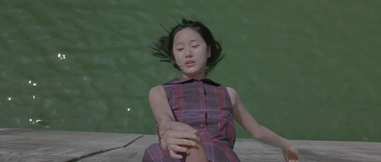 Oldboy (2003) movie still: medium — A stone ledge borders a expanse of dark, rippling water. A young woman lies horizontally on the concrete, gazing…