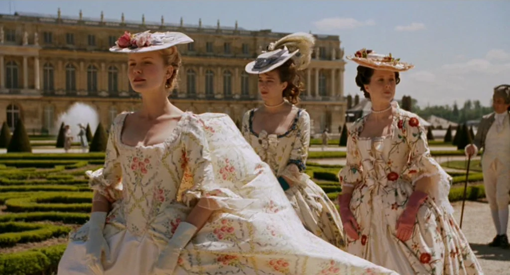 Marie Antoinette (2006) movie still: fullbody — Three women in 18th-century style dresses walk through the manicured grounds of a palace. A large…