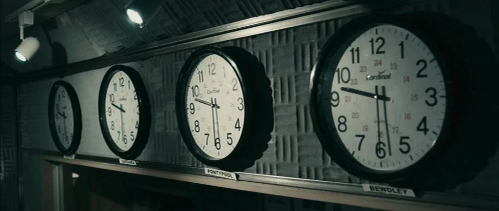 Pontypool (2008) movie still: medium — A radio studio wall is covered in acoustic foam and features four analog clocks. Each clock has a label…