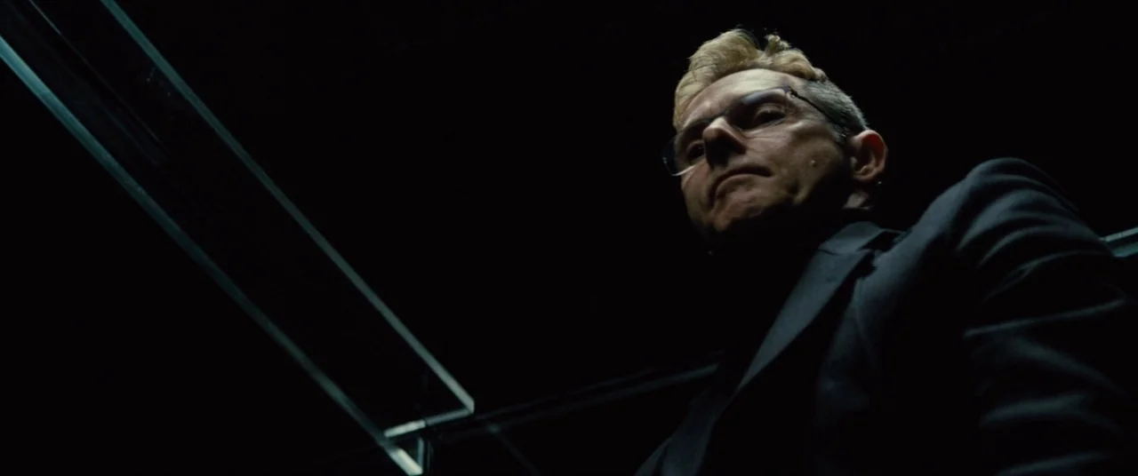 Mission: Impossible – Rogue Nation (2015) movie still: medium — A dark elevator interior with sharp lighting illuminating a man from above. The man…