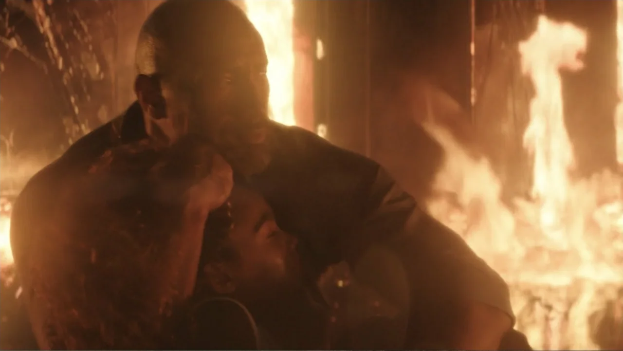 Skyscraper (2018) movie still: medium — A man holds an unconscious person amidst a room engulfed in bright orange flames. Intense fire illuminates…