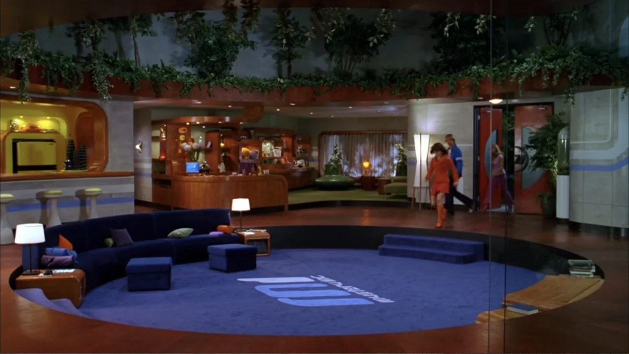 Scooby-Doo 2: Monsters Unleashed (2004) movie still: wide — A sunken circular lounge area features a deep blue rug and wood paneling walls. A young…