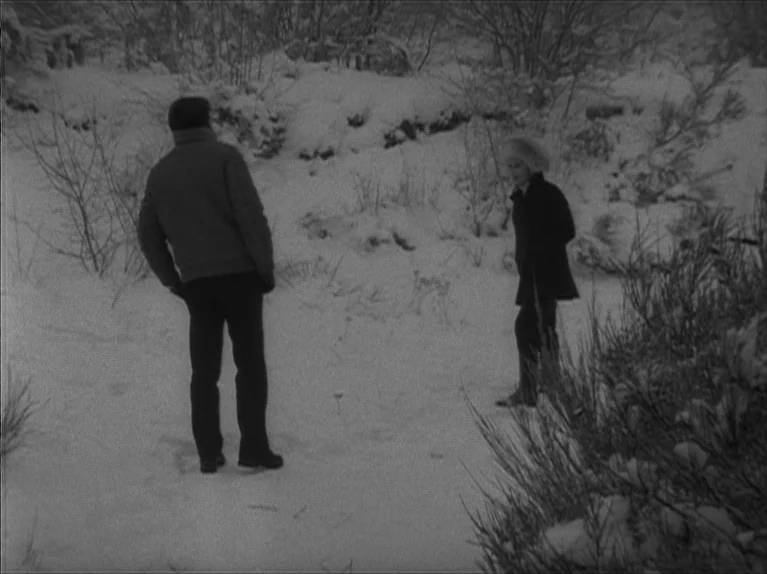 My Night At Maud’s (Ma Nuit Chez Maud) (1969) movie still: wide — A snow-covered clearing surrounded by thin trees and bare winter brush. A man and…