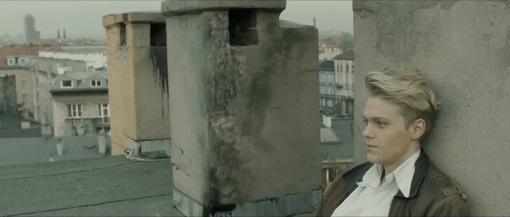 Lasting (Nieulotne) (2013) movie still: medium — A flat urban rooftop features several concrete chimneys against a background of city buildings. A…
