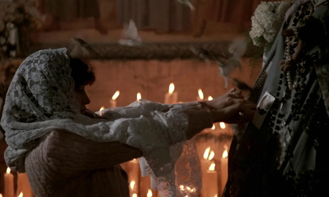 Nostalghia (1983) movie still: medium — A dark chapel interior is illuminated by numerous flickering candles on a shelf. A woman in a lace head…