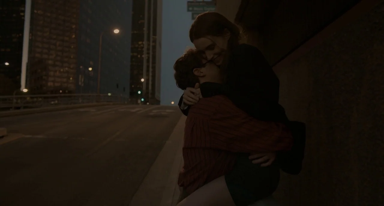 Her (2013) movie still: medium — A concrete urban overpass at night with distant city high-rises in the background. A man lifts a woman up in a hug…