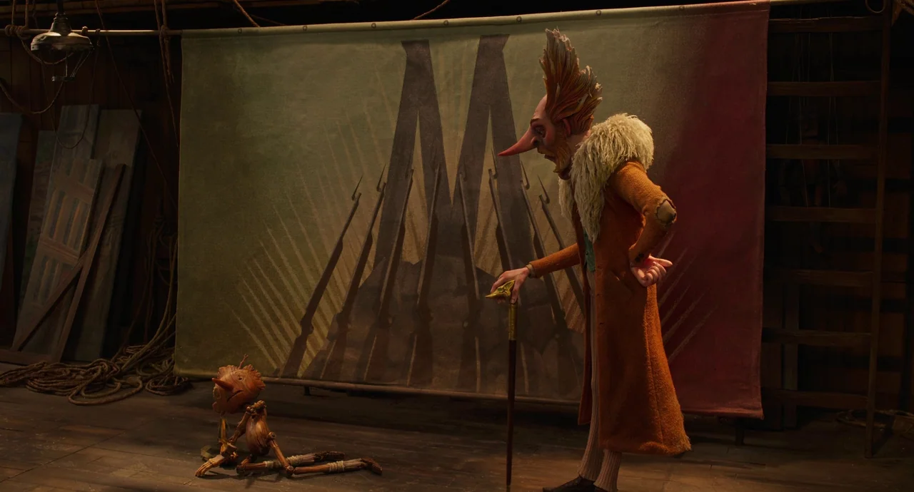 Guillermo del Toro’s Pinocchio (2022) movie still: fullbody — A wooden interior space features a large fabric banner depicting rifles and a stylized…