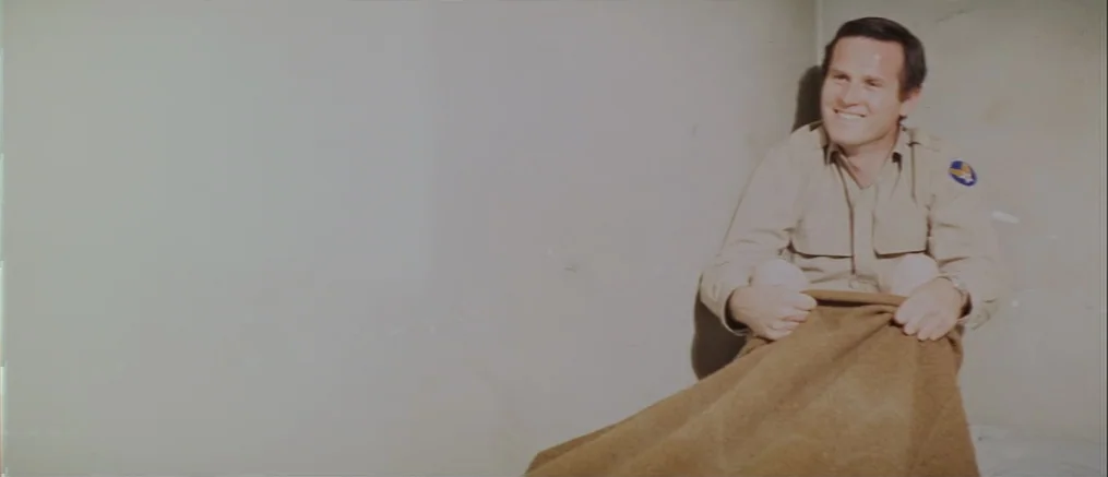 Catch 22 (1970) movie still: medium — A stark room with plain concrete walls provides a sterile, confined environment. A man in military-style…