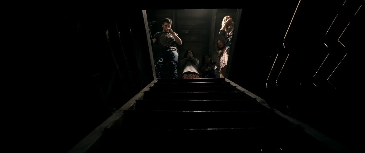 Evil Dead (2013) movie still: wide — Five individuals gather at the top of a dark wooden staircase in a house. They look down into the void while…