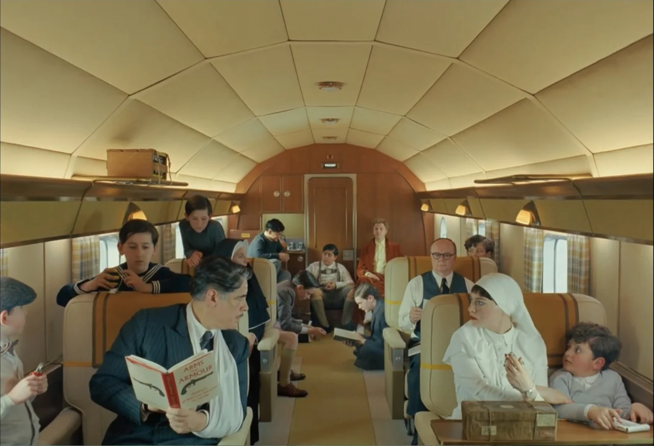 The Phoenician Scheme (2025) movie still: wide — The interior of a vintage passenger airplane with upholstered seats and wood paneling. Multiple…