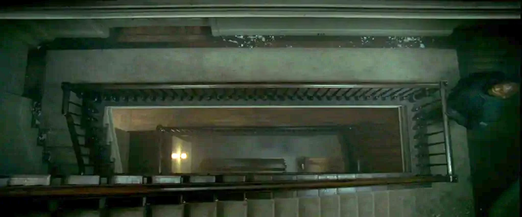 Panic Room (2002) movie still: establishing — A dark, vertical view looking directly down an old multi-story stairwell. The wooden banisters frame a…