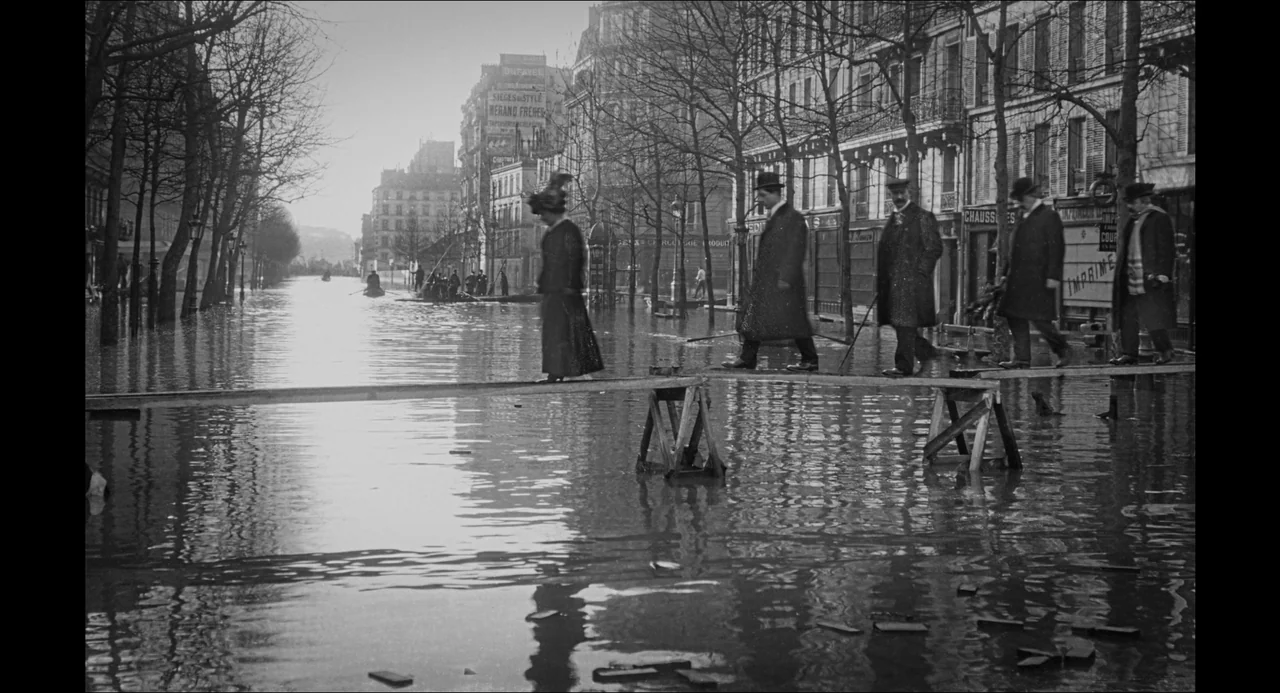Transformers: Rise of the Beasts (2023) movie still: wide — A Paris street is flooded with water, lined by leafless trees and storefronts. People…