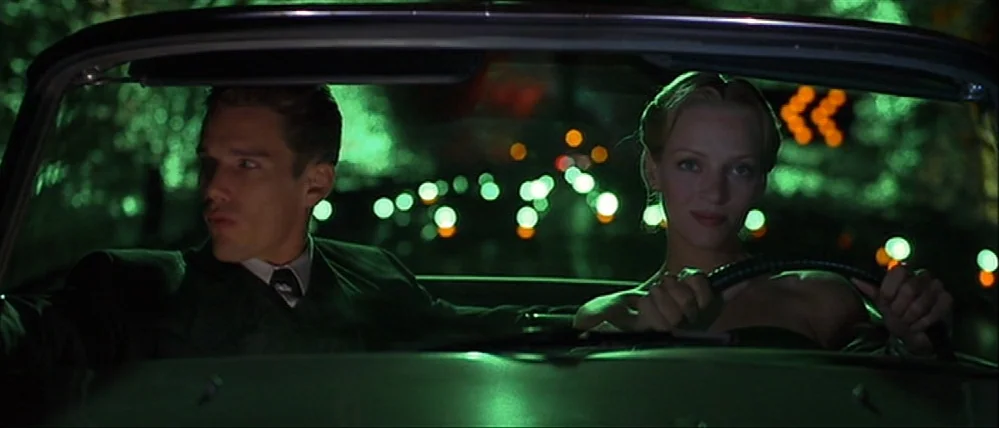 Gattaca (1997) movie still: medium — A man and a woman sit in the front seats of a dark vintage convertible. Green ambient city light reflects…