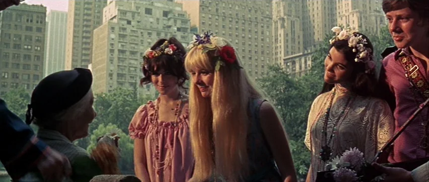 Sweet Charity (1969) movie still: medium — A group of young people wearing floral accessories stand together in a city park. Tall apartment…