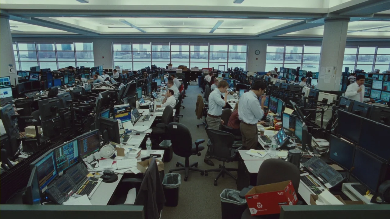 Margin Call (2011) movie still: wide — A sprawling financial trading floor features rows of desks cluttered with multiple computer monitors.…