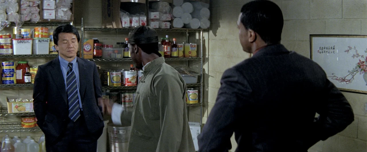 Rush Hour 2 (2001) movie still: medium — A cluttered storage room features metal wire shelves stacked with various food cans and jars. Three men…