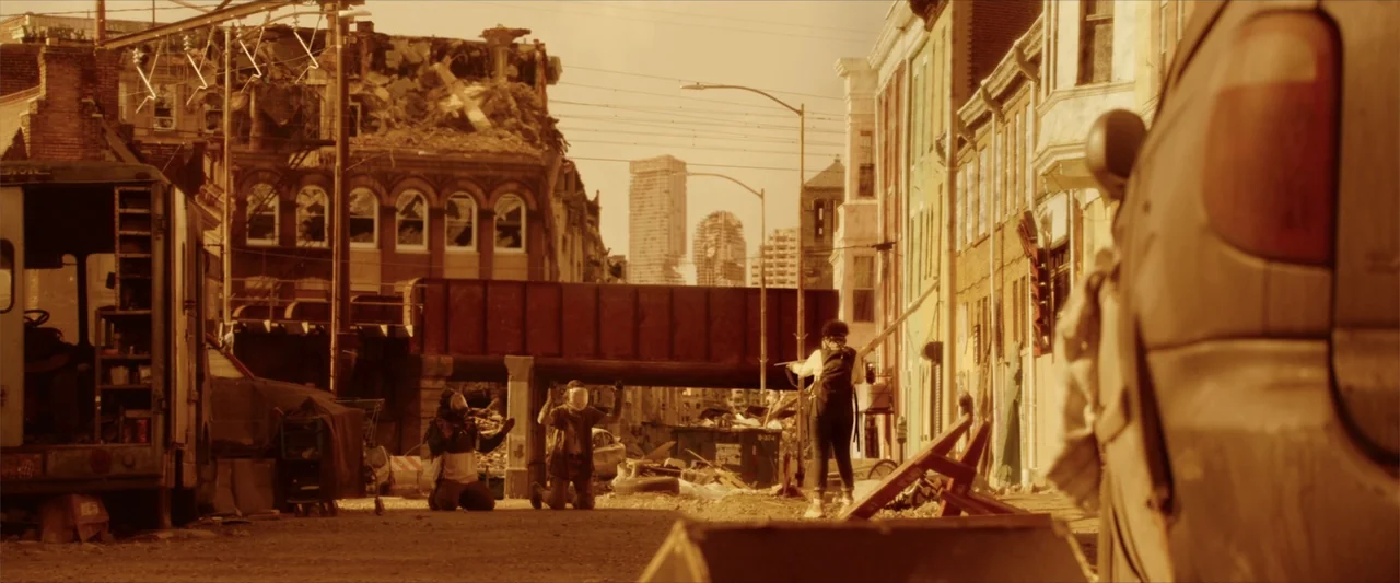 Breathe (2011) movie still: wide — A devastated city intersection features crumbling brick buildings and a rusted railway overpass. Three…