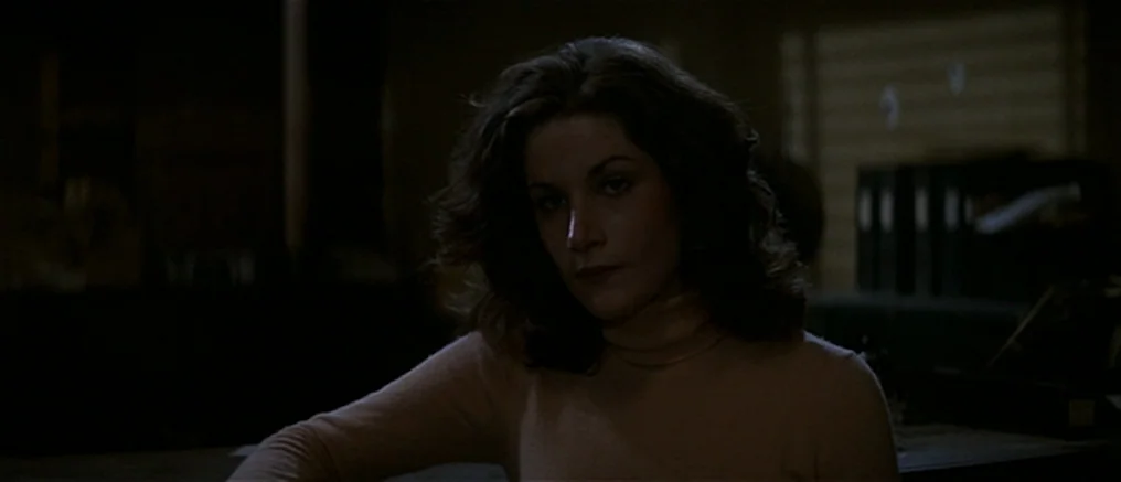 Assault on Precinct 13 (1976) movie still: medium — A dimly lit room with rows of dark filing cabinets in the background. A woman sits behind a desk…