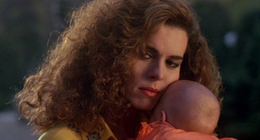 Matador (1986) movie still: closeup — An outdoor setting with out-of-focus greenery and warm sunlight during the golden hour. A woman with curly…