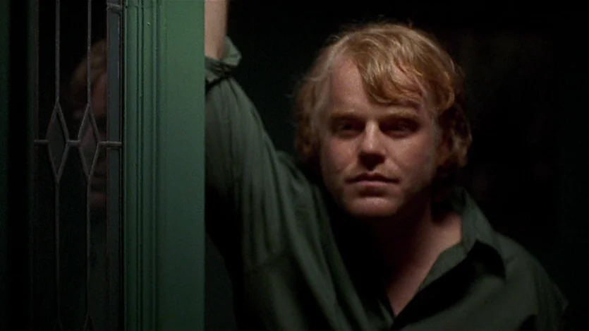 Love Liza (2002) movie still: medium — A dimly lit interior shows a person leaning against a decorative green door frame. The subject stands in the…