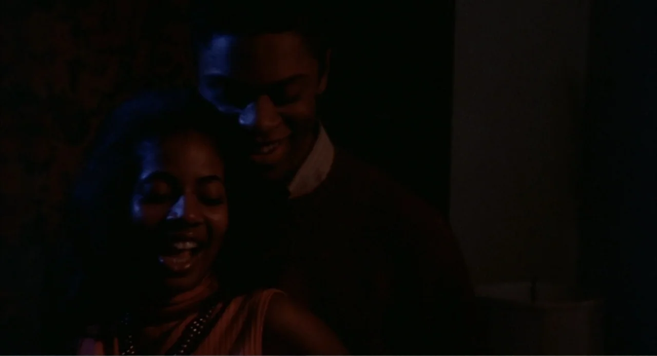 Cooley High (1975) movie still: medium — An interior space at night with dark shadows and visible textures on the wall. A man stands closely behind…
