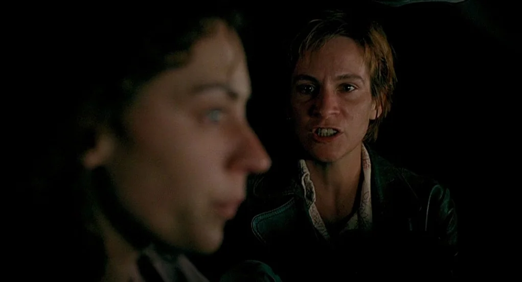 Butterfly Kiss (1995) movie still: medium — The interior of a dark car at night with no visible external light. A woman is speaking intensely to…