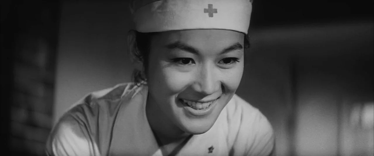 The Human Condition II: Road to Eternity (1959) movie still: closeup — A dimly lit indoor space with a focus on a medical worker's face. The nurse…