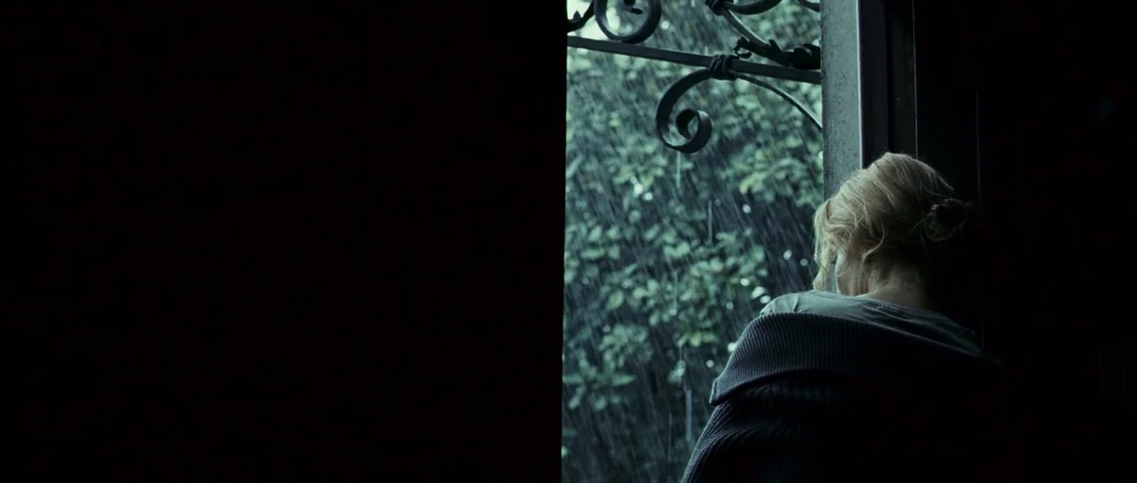 The Orphanage (2007) movie still: medium — An interior space features an open window looking out toward a heavy rainstorm. A woman stands in the…