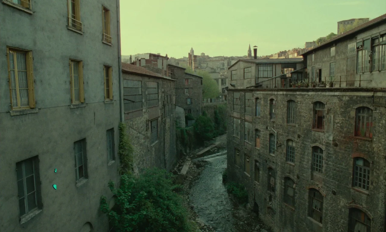 Litan (1982) movie still: establishing — A narrow stone canal runs through an old European town between multi-story buildings. Weathered masonry…