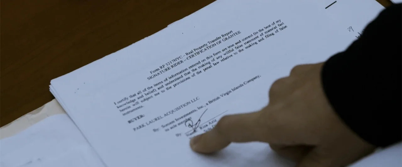 The Kleptocrats (2018) movie still: closeup — A legal document labeled Real Property Transfer Report sits on a dark desk surface. A finger points…