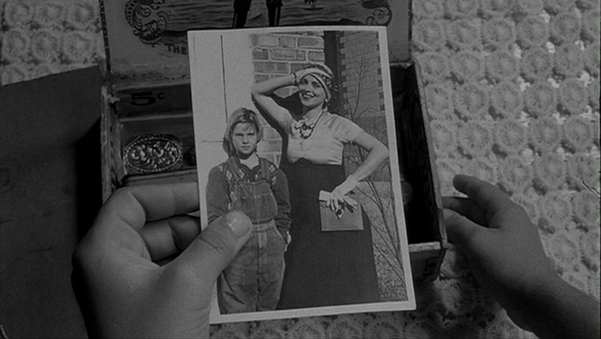 Paper Moon (1971) movie still: closeup — A pair of hands holds a vintage black and white photograph over an open box. The box sits atop a crocheted…