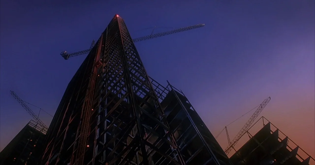 Darkman (1990) movie still: establishing — A tall steel building frame rises against a twilight sky with construction cranes. Several tower cranes…