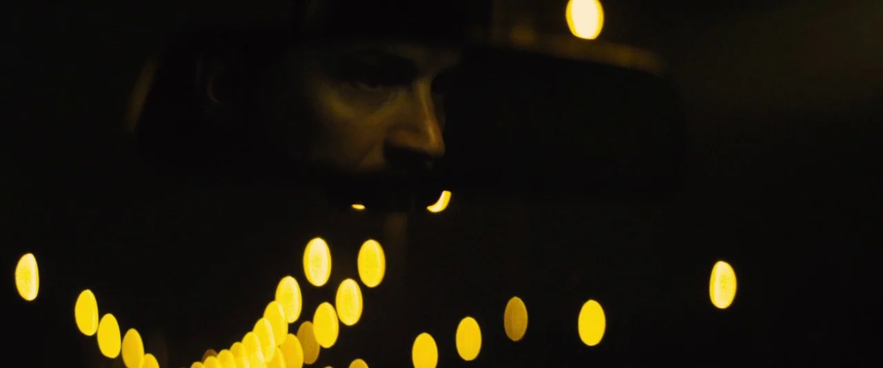 Locke (2013) movie still: closeup — The interior of a vehicle at night is engulfed in darkness. A man's partially illuminated face is visible behind…