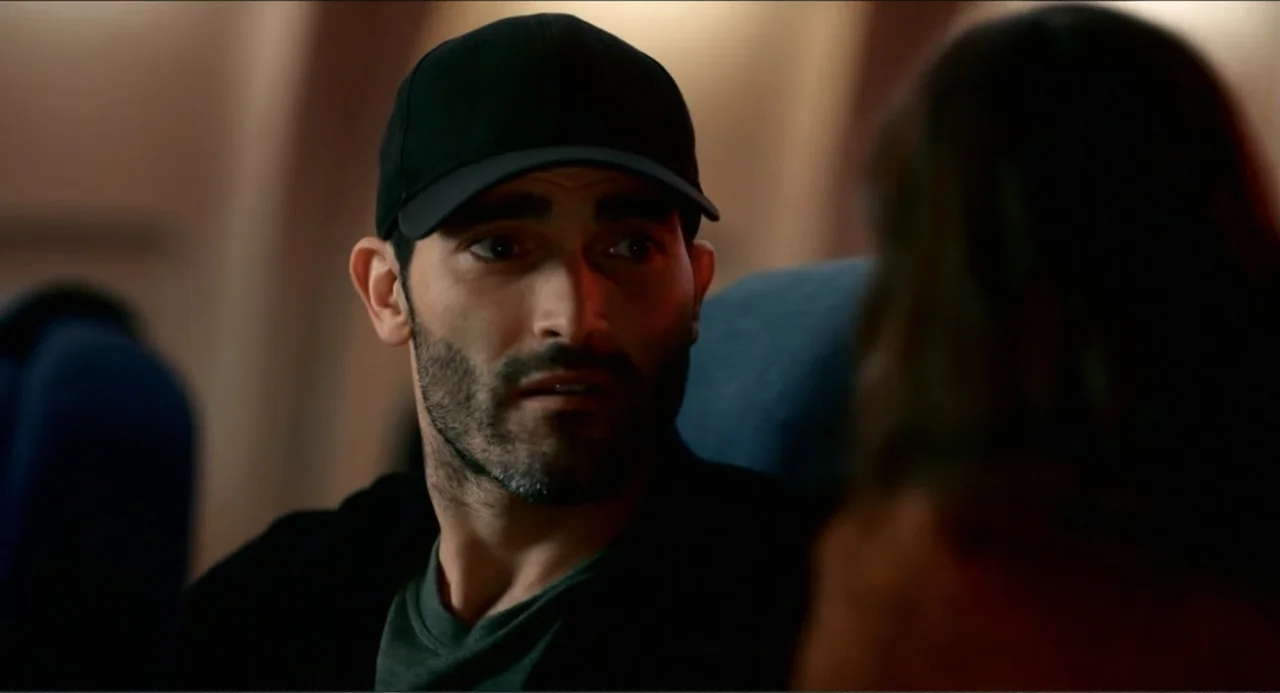 Can You Keep a Secret? (2019) movie still: closeup — An interior airplane cabin with dark seating in a dim, enclosed environment. A man in a…