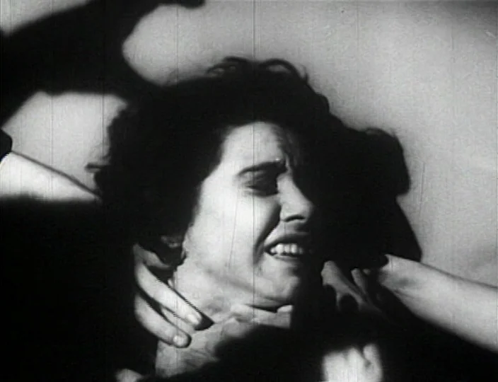 Dementia (Daughter of Horror) (1955) movie still: closeup — A dimly lit, high-contrast interior scene with a stark background. A woman's face is…