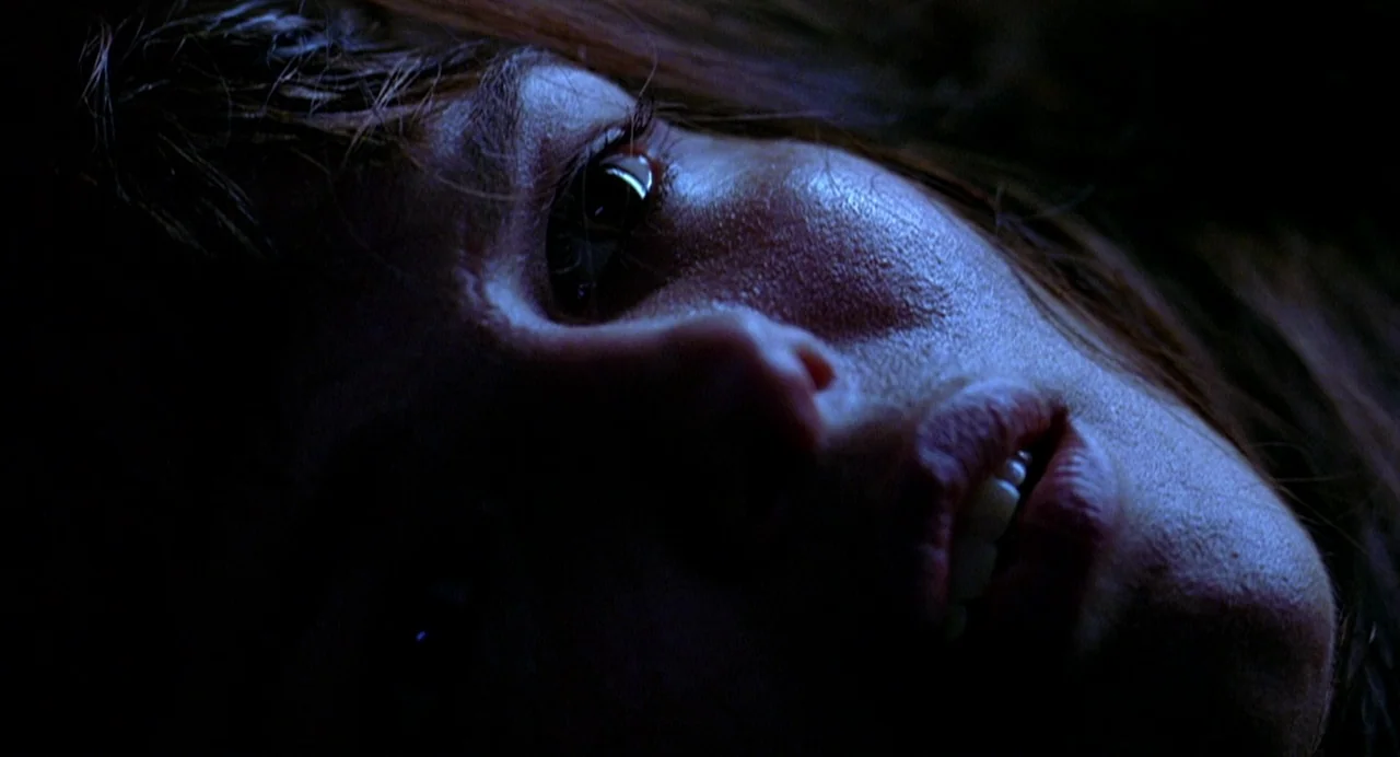 Office Killer (1997) movie still: closeup — A close-up view shows a person's face positioned in dark and low-light conditions. The subject lies…