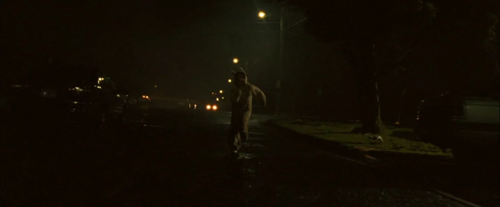 Where The Wild Things Are (2009) movie still: wide — A dark, wet residential street at night illuminated by distant orange streetlights. A person…
