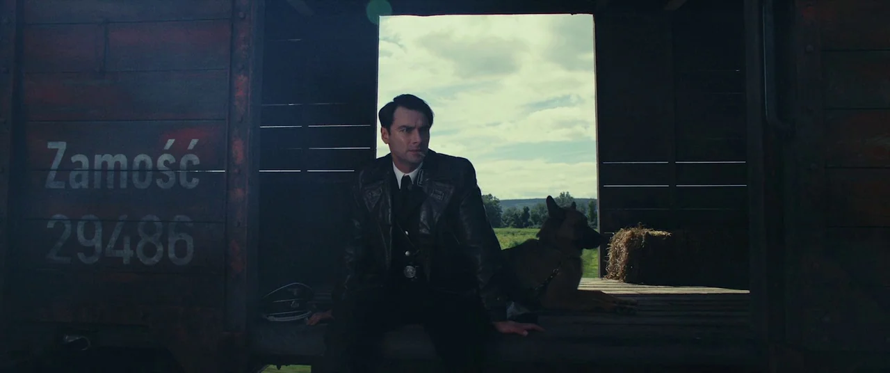 The Man Who Killed Hitler and Then the Bigfoot (2018) movie still: medium — A dark wooden train boxcar marked Zamość and 29486 sits open to a field.…
