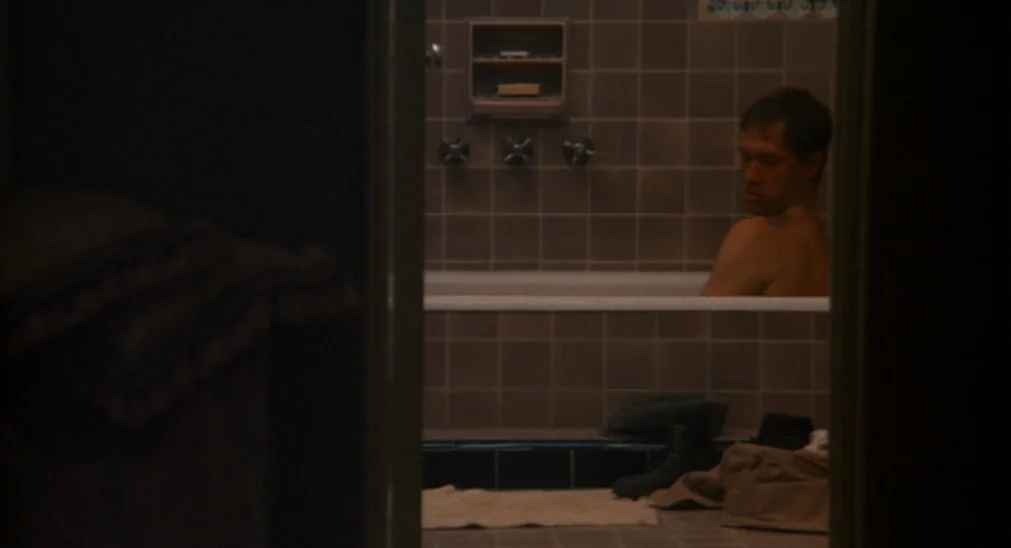 Bound For Glory (1976) movie still: medium — A dimly lit room features a tiled tub area seen through a doorway. A man sits submerged in the water…